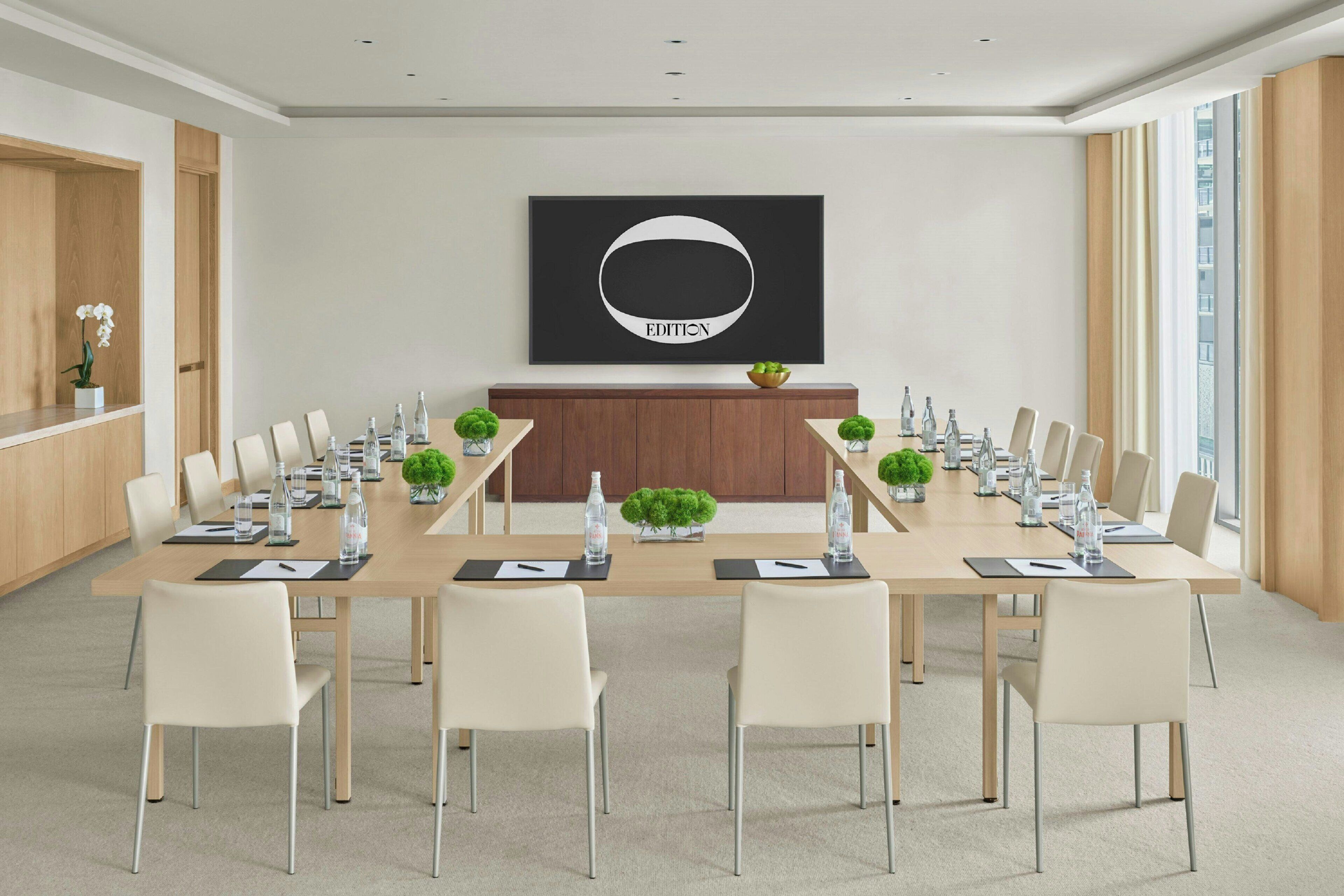 A conference room with a long table, chairs, water bottles, and a plant on the table.