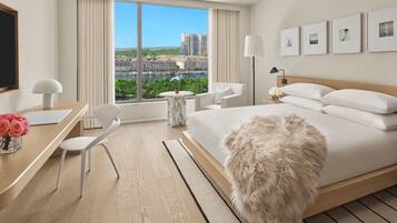A modern hotel room with a large bed, a desk, a chair, and a view of the cityscape.