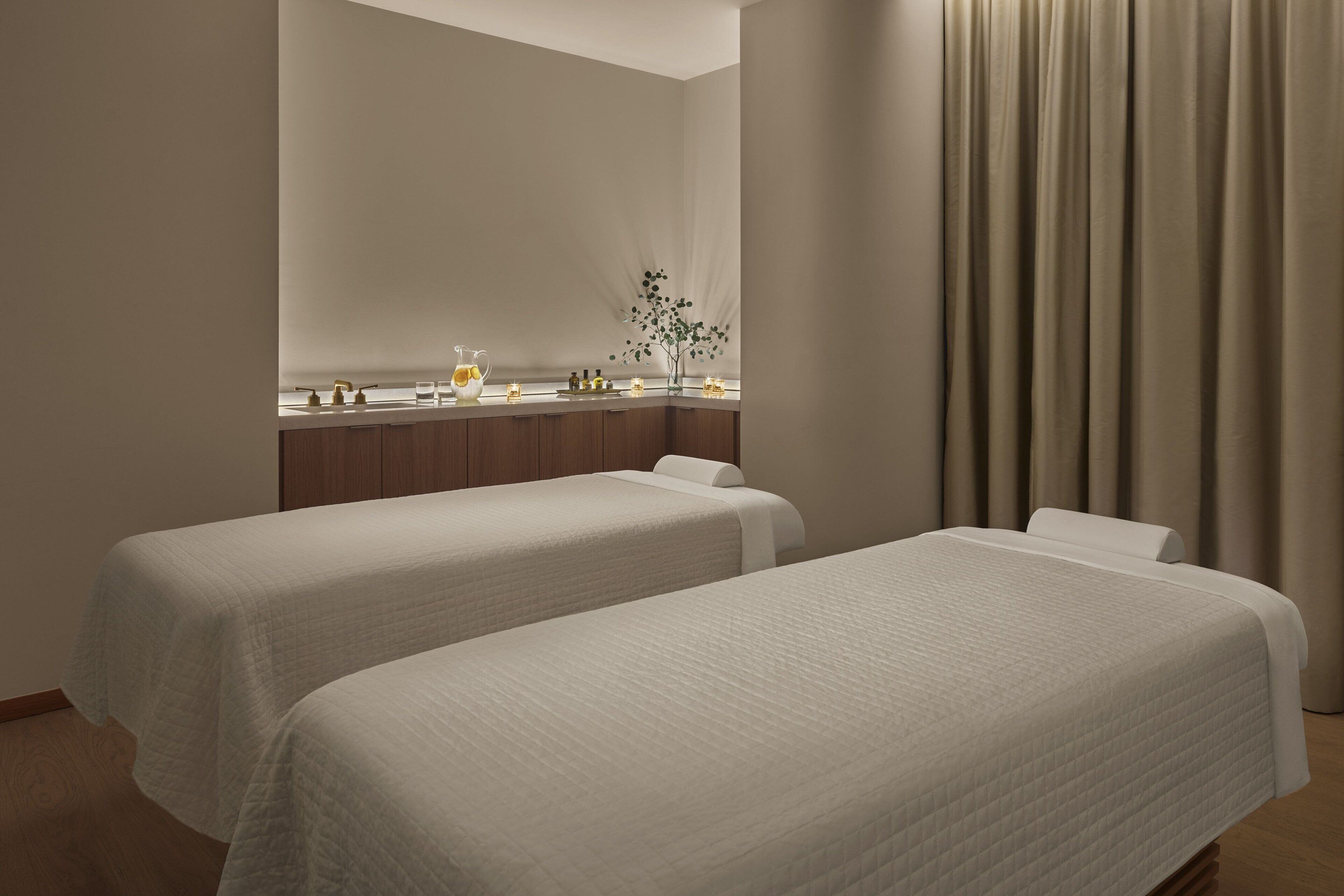 A hotel room with two beds, a vanity with toiletries, and a window with curtains.