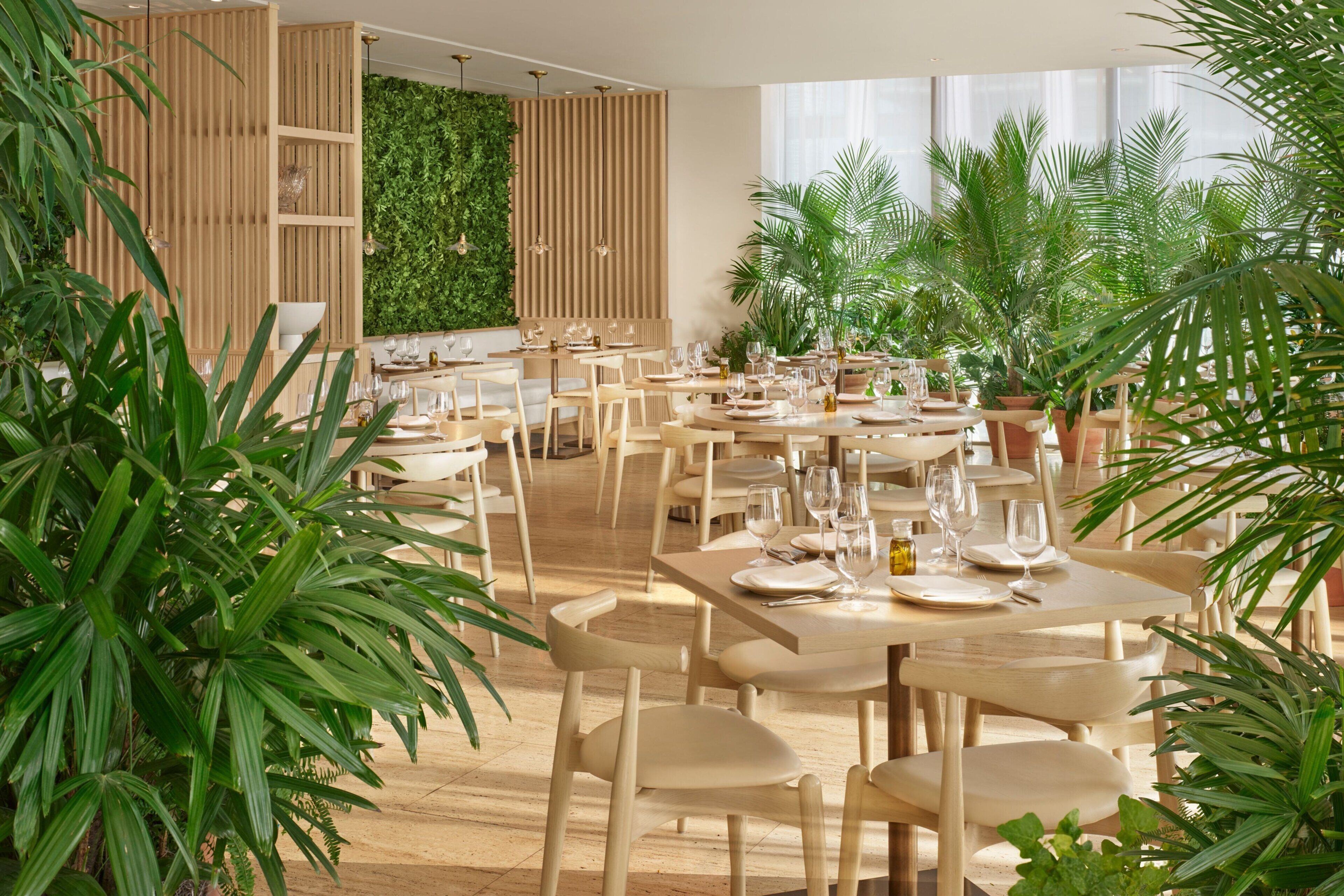 Un restaurante con mesas y sillas de madera, plantas verdes y una pared con listones verticales de madera.
