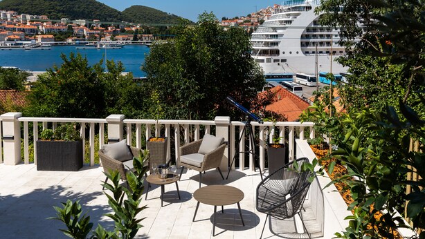 Un balcon agrémenté de meubles en osier, avec vue sur un navire de croisière et, au loin, sur une ville côtière.