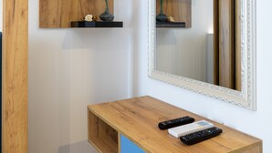 Une coiffeuse en bois avec un miroir, deux horloges et un vase rempli de fleurs roses.