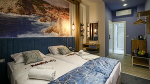 Une chambre d’hôtel avec un grand lit, un tableau représentant un paysage côtier, une table de chevet en bois et une armoire.