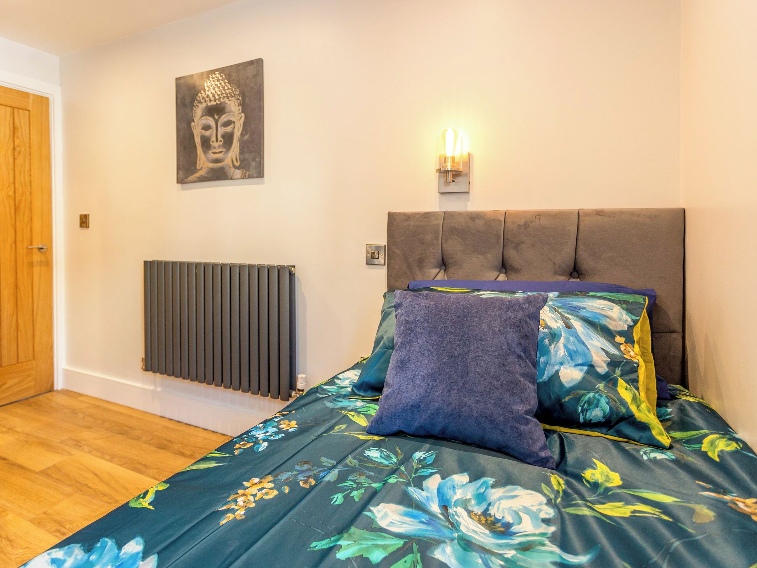 Un dormitorio con cama, un radiador, una lámpara de pared y una estatua de Buda.