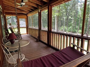 Une terrasse en bois avec un coin salon doté de coussins, une table avec des chaises et une vue sur une forêt.
