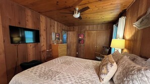 A room with a bed, a ceiling fan, a television mounted on the wall, a wardrobe, and a desk with a chair. - Cozy Cabin in the Woods, near Carolina Horse Park (Raeford)