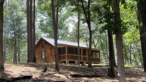 A cabin in a forest with a wooden exterior, large windows, and a deck. - Cozy Cabin in the Woods, near Carolina Horse Park (Raeford)