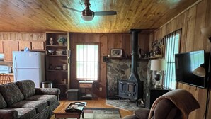 A cozy living room with a sofa, armchair, coffee table, fireplace, television, and wooden walls. - Cozy Cabin in the Woods, near Carolina Horse Park (Raeford)