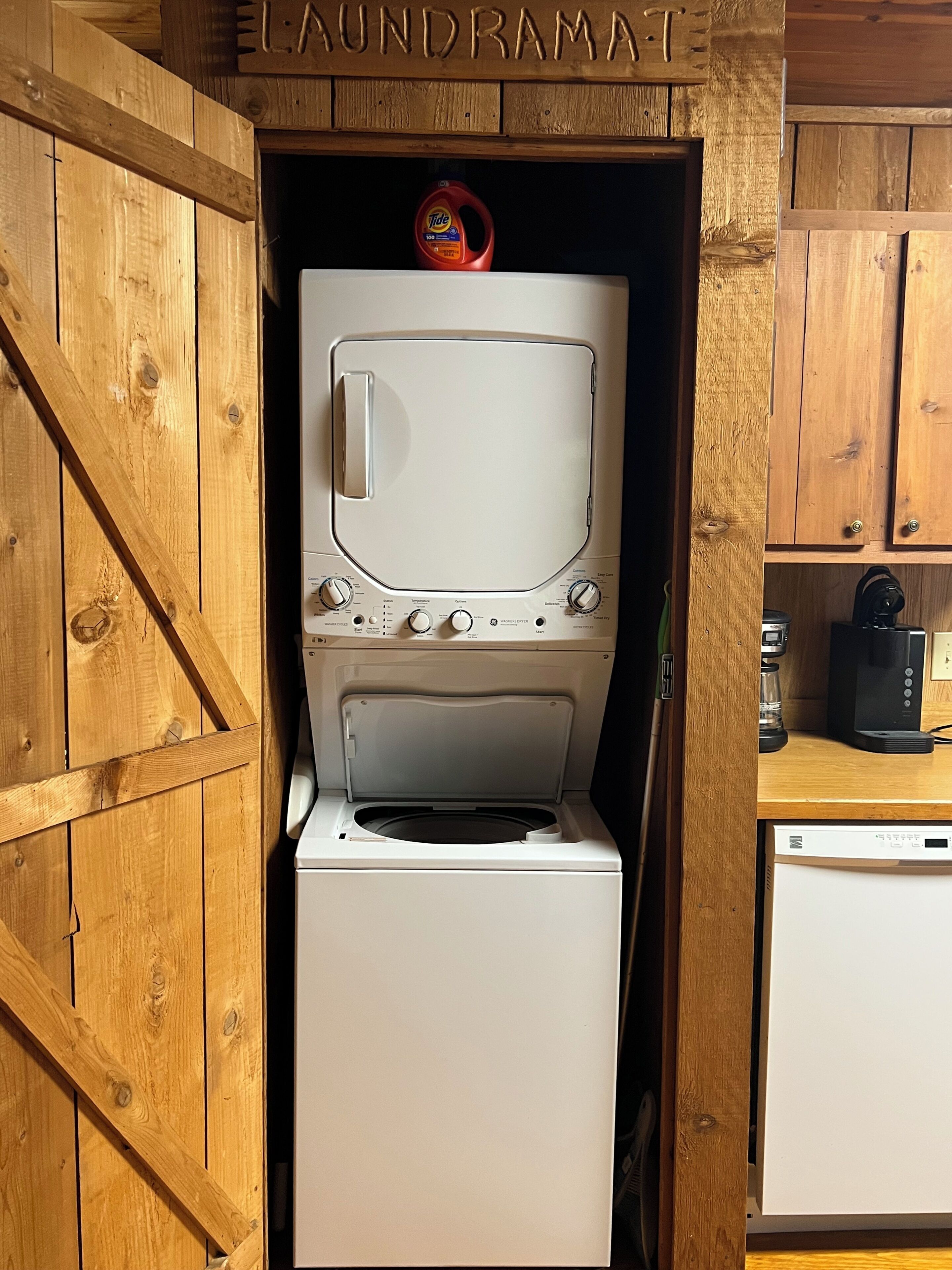 A laundry room with a washing machine and dryer, wooden cabinets, and a sign above the dryer reading 'LAUNDRAMAT'.