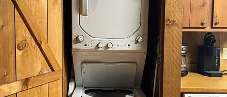 A laundry room with a washing machine and dryer, wooden cabinets, and a sign above the dryer reading 'LAUNDRAMAT'.