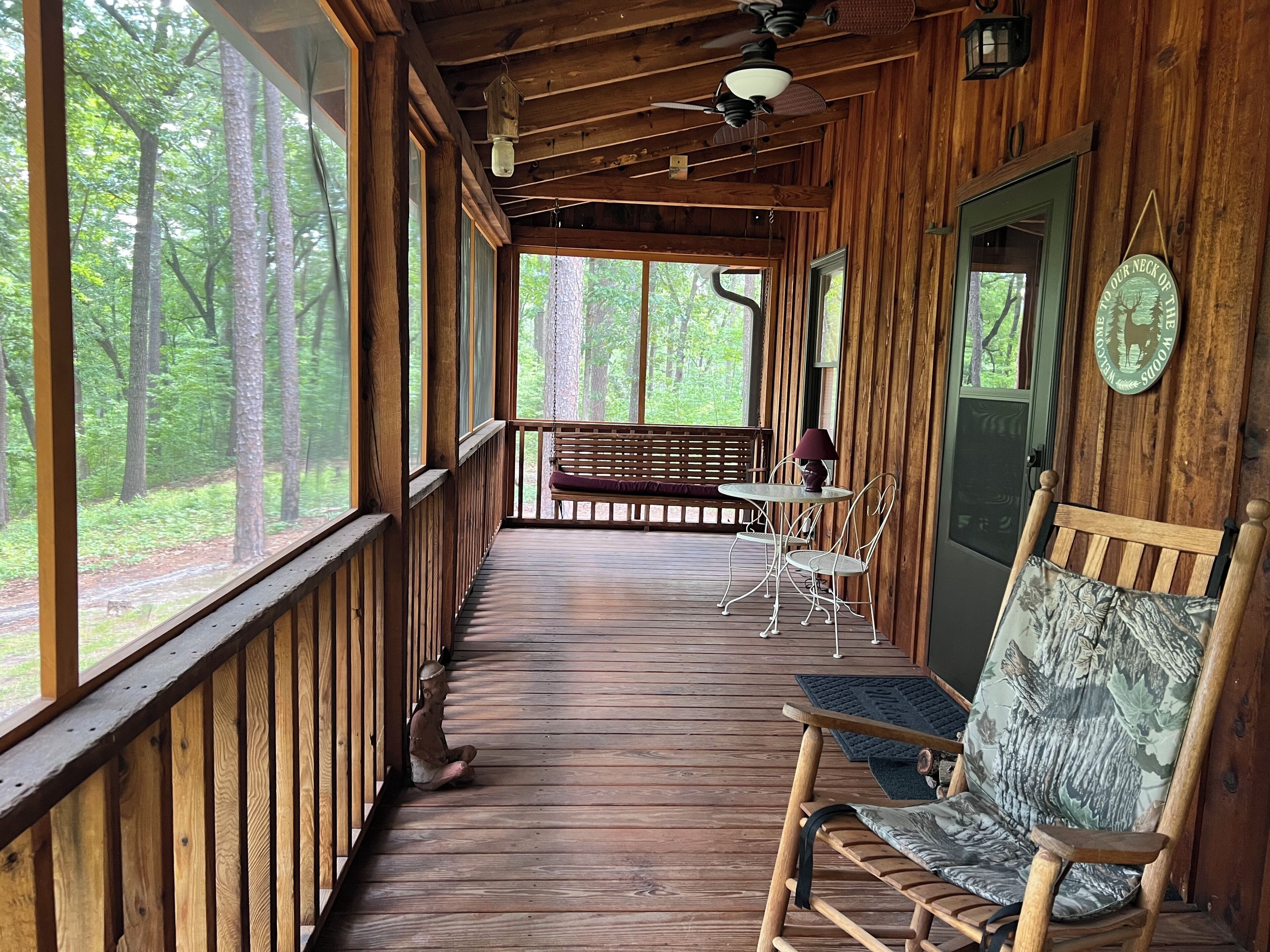 A wooden cabin with a porch, a bench, a table with chairs, and a door with a sign.