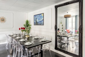 Comedor con una larga mesa dispuesta para una comida, sillas transparentes y un espejo grande.