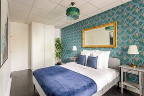 Un dormitorio con una cama, una mesita de noche, una lámpara, un espejo y una planta en maceta.