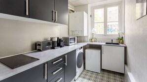 Een kleine keuken met een ingebouwde magnetron, broodrooster en koffiezetapparaat. Er is een klein spoelgedeelte en een raam met uitzicht op groen.