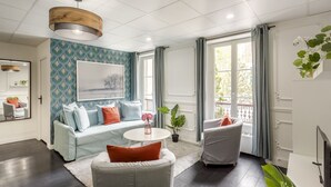 Een moderne woonkamer met een bank, twee fauteuils, een ronde salontafel en een groot raam met gordijnen.