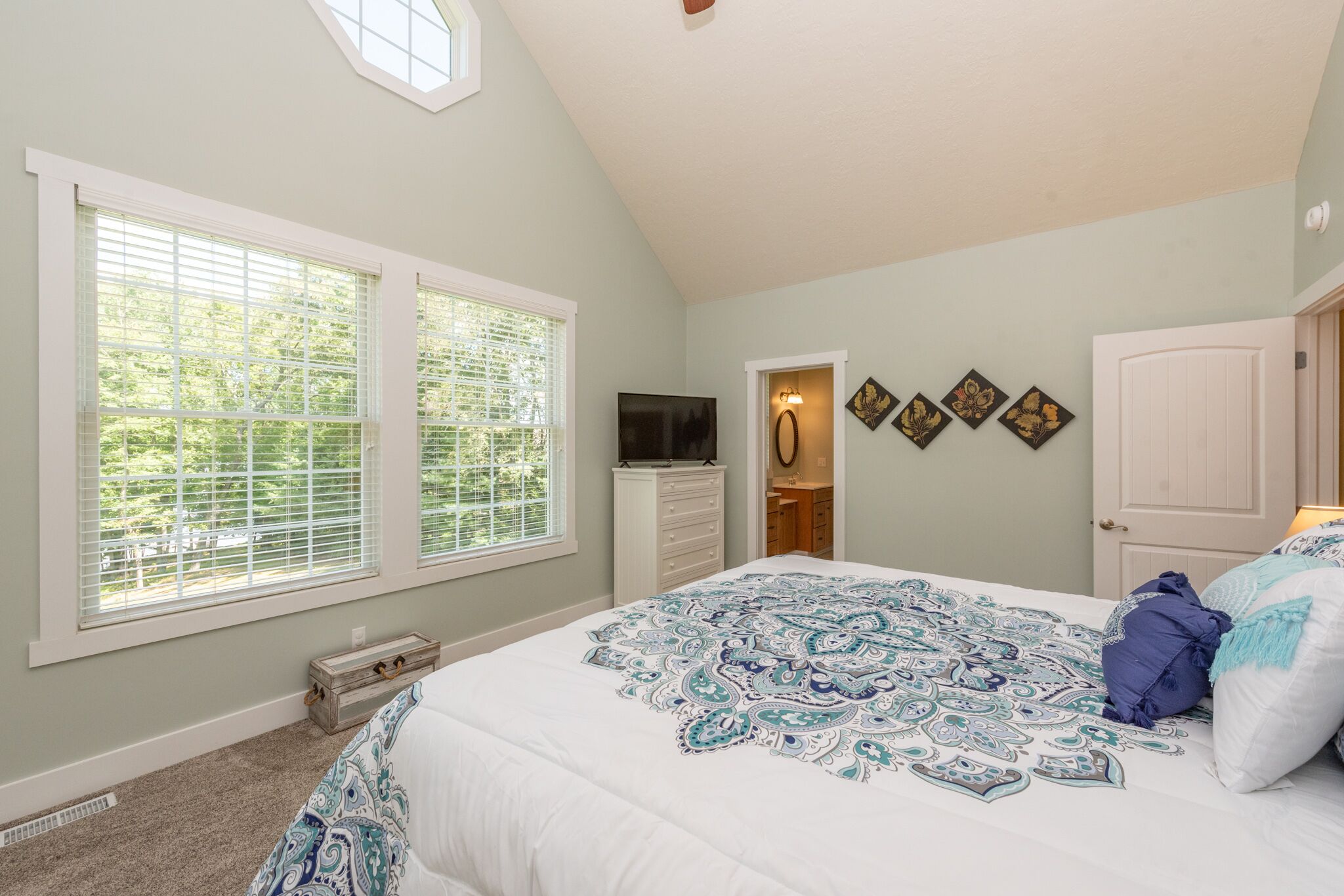 A bedroom with a large bed, a dresser, a television, and a window with blinds.