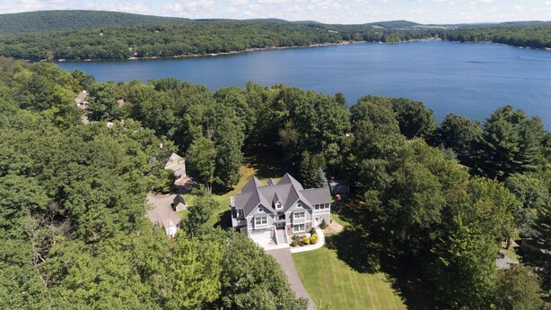 Ein großes, zweistöckiges Haus mit einer umlaufenden Veranda, umgeben von dichtem Wald und einem See.