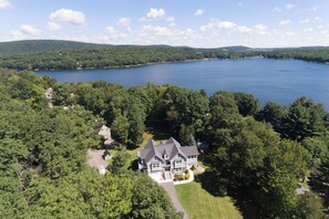A large, two-story house with a wrap-around porch, surrounded by dense forest and a lake. - Luxury Lake Escape w/ Hot Tub & Fire Pit (Oakland)