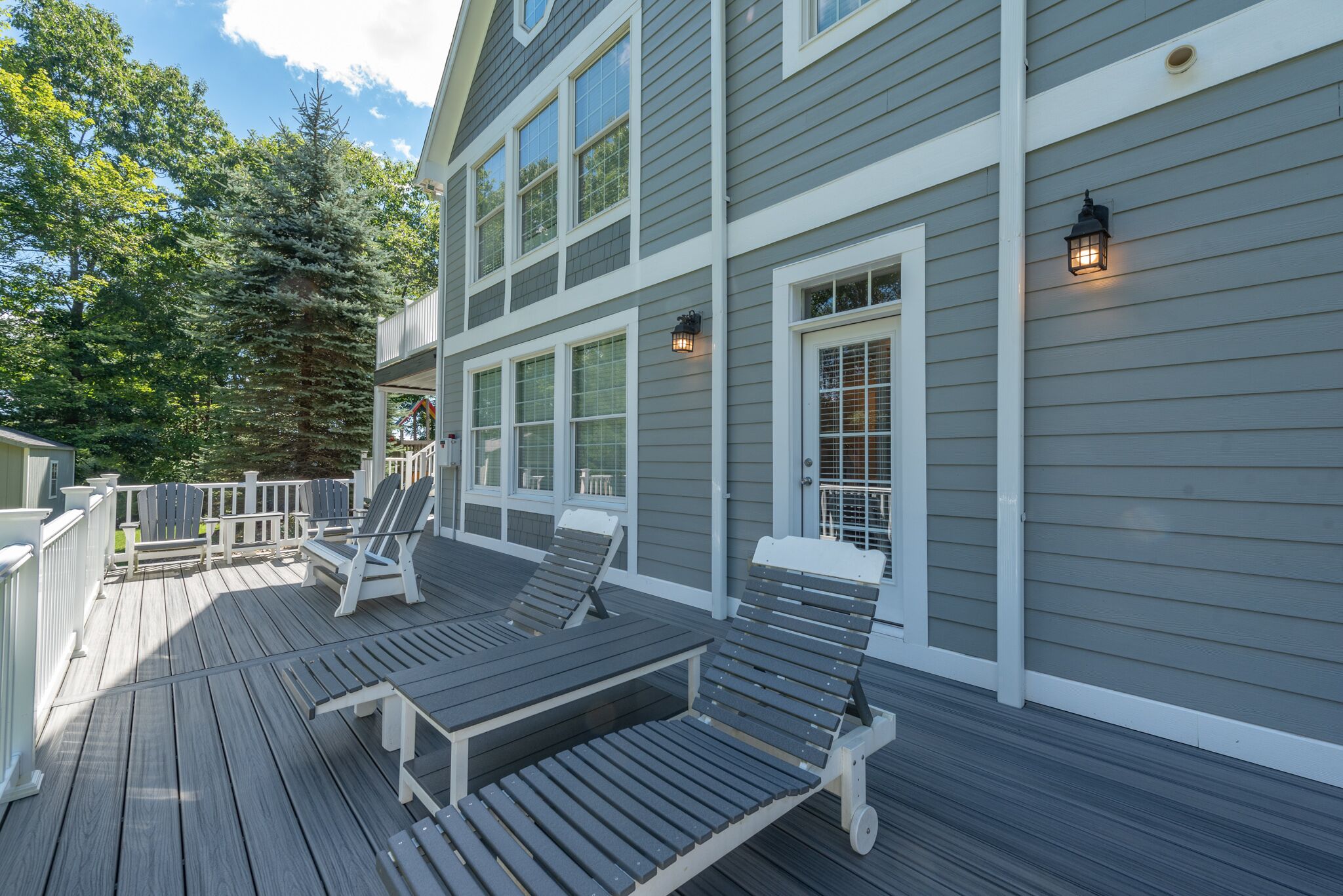 A deck with lounge chairs and a railing, overlooking a forested area.