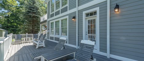 A deck with lounge chairs and a railing, overlooking a forested area.