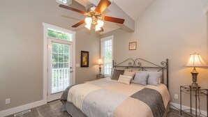 Ein Schlafzimmer mit Bett, Deckenventilator, zwei Fenstern und einem Nachttisch mit Lampe.