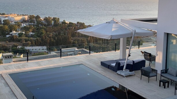 Un espace piscine extérieur moderne offrant une vue sur la mer et les montagnes lointaines.
