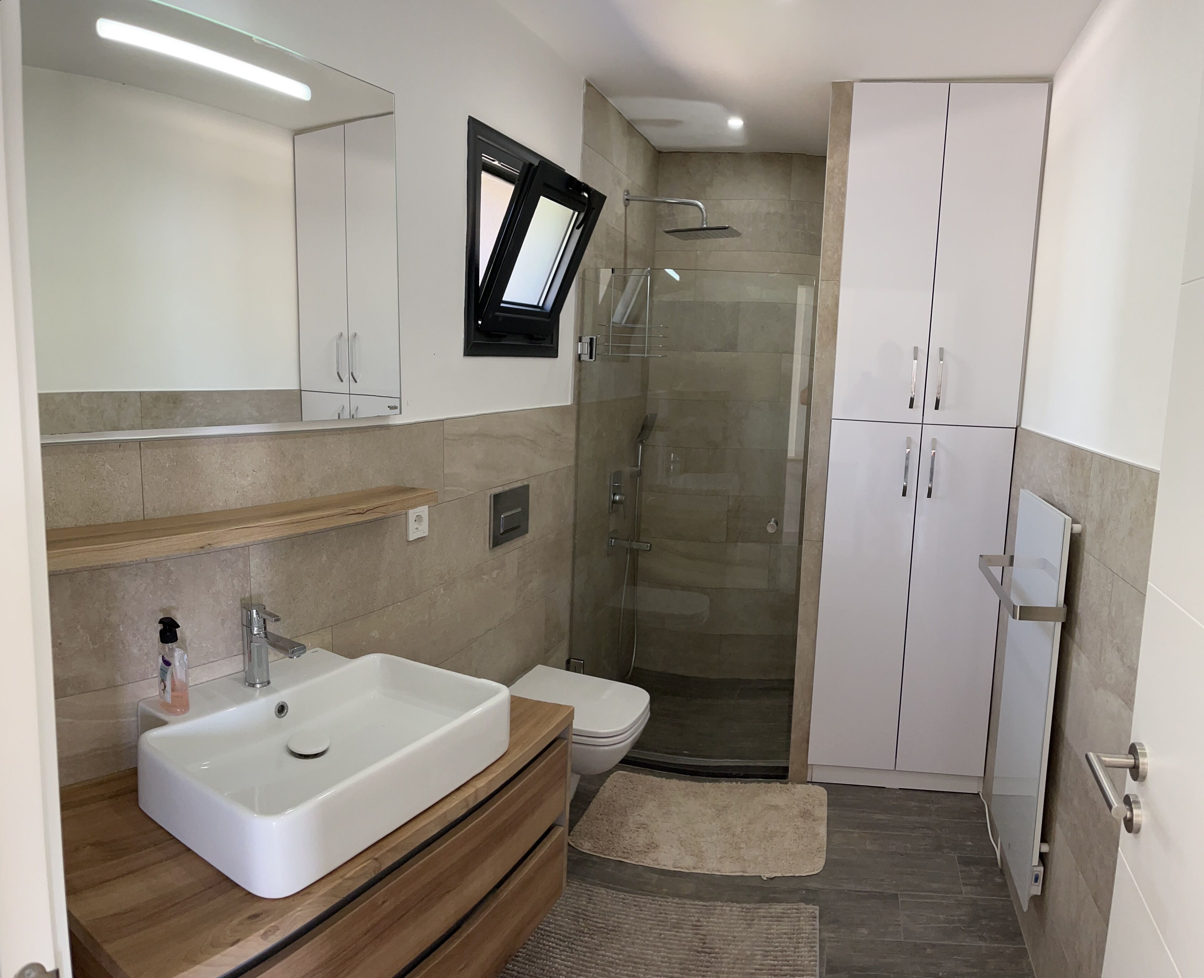 A modern bathroom with a large sink, mirror, shower, and toilet.