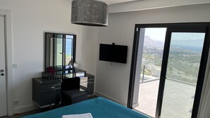 Une chambre moderne avec balcon, une coiffeuse avec miroir, une télévision à écran plat et des serviettes soigneusement pliées sur le lit.