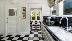 A kitchen with a black and white checkered floor, a white door, and a window with curtains.