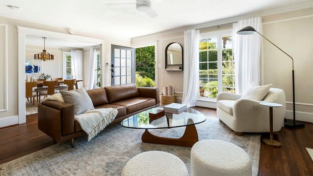A spacious living room with a brown leather sofa, a white armchair, a glass coffee table, and a round rug.