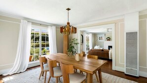 A dining area with a wooden table and chairs, a hanging light fixture, and a view of the outdoors through large windows.