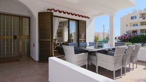 Um pátio externo com mesa e cadeiras de jantar, uma porta de vidro deslizante e vista para os edifícios ao redor.