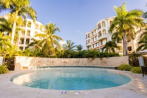 Ein Swimmingpool, umgeben von Palmen und einem Gebäude mit mehreren Balkonen.