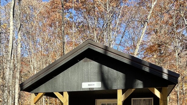 Una cabaña de madera con un porche, una puerta y un letrero que dice "BEECH".