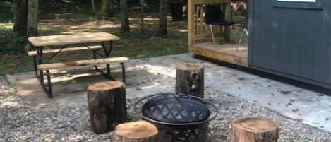 A rustic outdoor seating area with a picnic table, fire pit, and wooden stumps.