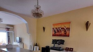 Un comedor con una mesa y sillas, una araña, un cuadro y un aparador con adornos.