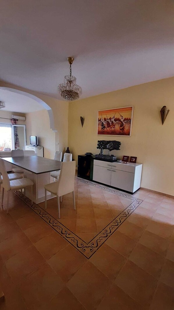 A dining area with a table and chairs, a chandelier, a painting, and a cabinet with decorative items.