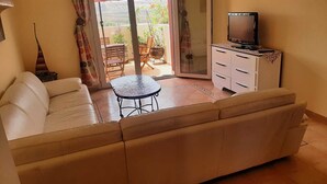 Un salón con sofá, una mesita, un televisor sobre un mueble, y vistas al balcón exterior.