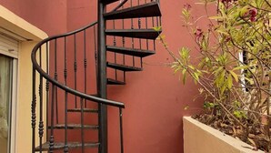 Una escalera de caracol en un patio con una pared roja y una planta en maceta.