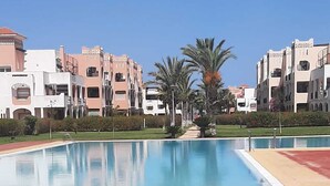 Una piscina con piso rojo, rodeada de edificios con balcones y palmeras.