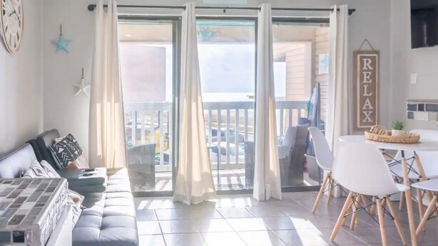 Ein Wohnzimmer mit einer Couch, einem Esstisch mit Stühlen und einem Balkon mit Vorhängen.