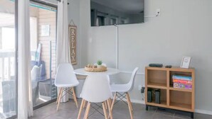 Ein modernes Wohnzimmer mit einem runden Tisch, weißen Stühlen, einem an der Wand montierten Fernseher und einem Holzregal.