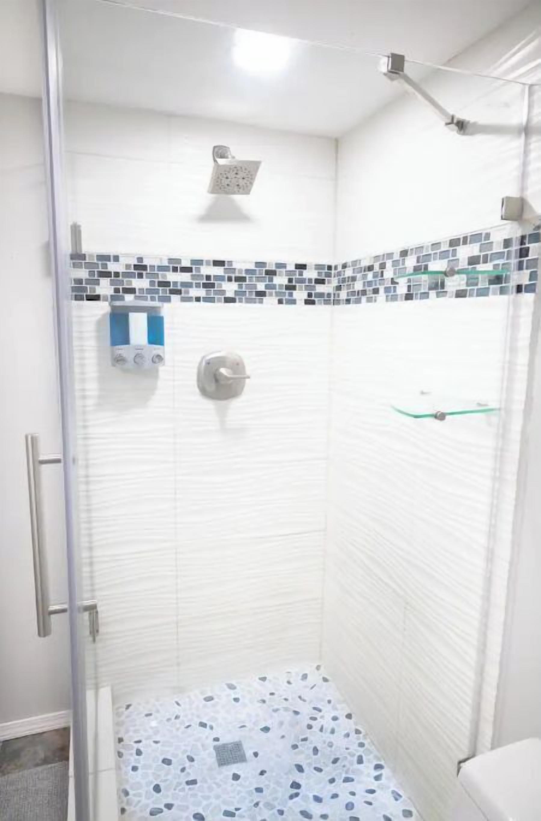 A shower with a glass door, a tiled floor, and a showerhead.
