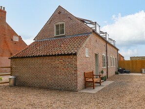 A small brick building with a sloped roof, a wooden bench, and a gravel driveway. - The Hayloft at Warren House (Market Rasen)