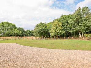 A fenced outdoor area with gravel, surrounded by trees and a wooden fence. - The Hayloft at Warren House (Market Rasen)