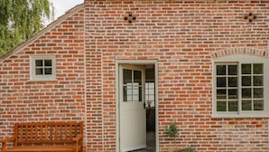 A brick building with a wooden bench, a door, and potted plants. - The Hayloft at Warren House (Market Rasen)
