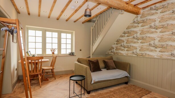 A cozy room with a wooden ceiling, a sofa with cushions, a small round table, and a chair. - The Hayloft at Warren House (Market Rasen)