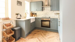 A modern kitchen with grey cabinets, a built-in oven, and a herringbone wooden floor. - The Stable at Warren House (Market Rasen)