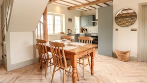 A dining area with a wooden table and chairs, a kitchen in the background, and a herringbone-patterned floor. - The Stable at Warren House (Market Rasen)