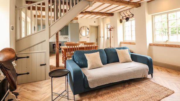 A cozy living room with a blue sofa, wooden flooring, and a staircase leading to a kitchen. - The Stable at Warren House (Market Rasen)